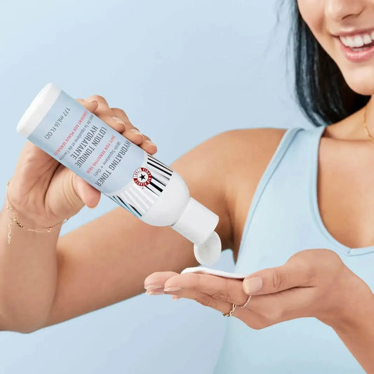 A person pouring First Aid Beauty Ultra Repair Wild Oat Soothing Toner into their palm, showcasing its hydrating formula.
