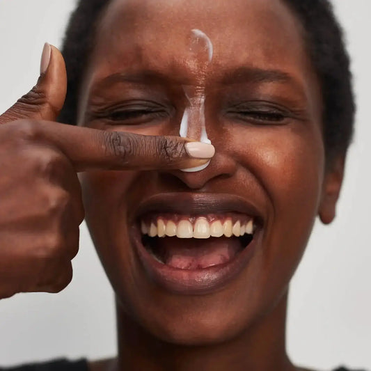Smiling woman applying moisturizer to her face, showcasing the INKEY List Vitamin B, C, and E Moisturizer.