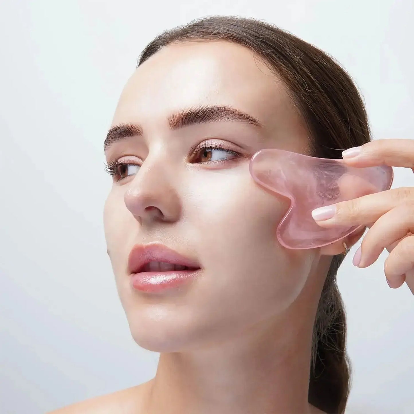 Woman using Brushworks Rose Quartz Gua Sha on her face for skincare and reducing puffiness.