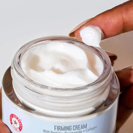 First Aid Beauty Firming Cream with Peptides, Niacinamide, and Collagen in a jar, demonstrating its creamy texture.