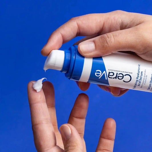 CeraVe Hydrating Hyaluronic Acid Serum 30ml being dispensed onto a finger against a blue background.