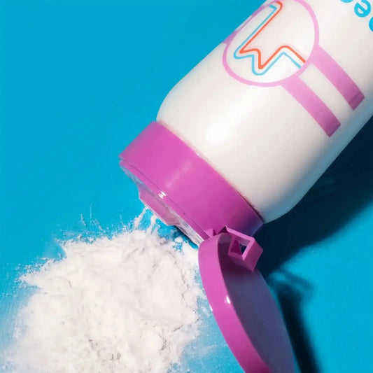 Container of Megababe Body Dust Powder spilling on a bright blue surface, showcasing its talc-free formula.