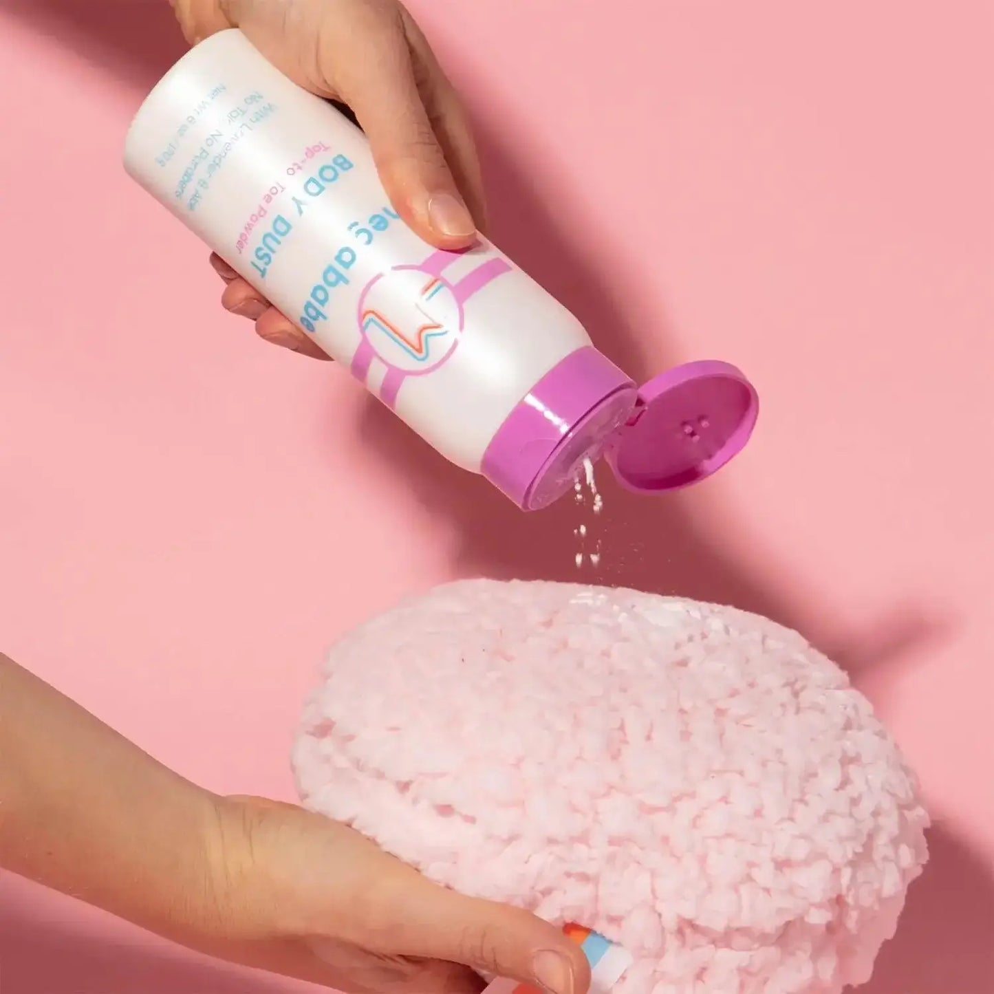Person pouring Megababe Body Dust powder onto a fluffy pink surface for easy application.
