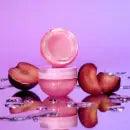 Glow Recipe Plum Hyaluronic Gloss Balm in jar with fresh plums on a reflective surface, vibrant purple background.