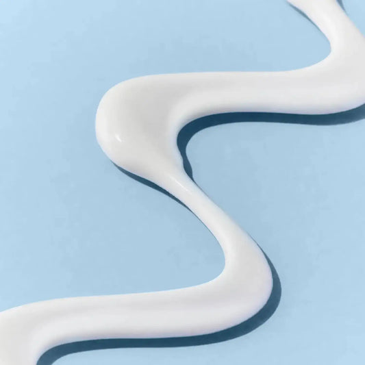 Close-up of a smooth, white cream swirled on a light blue background, ideal for skincare products.