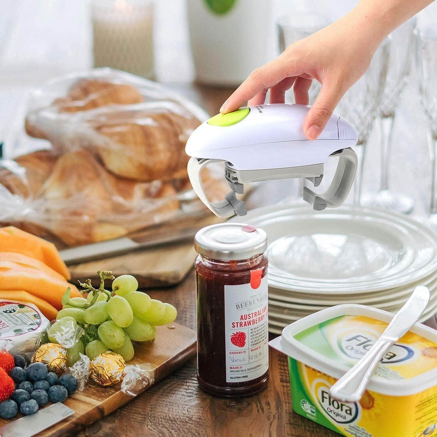 Electric jar opener effortlessly gripping a jar amidst a kitchen spread with food and plates.