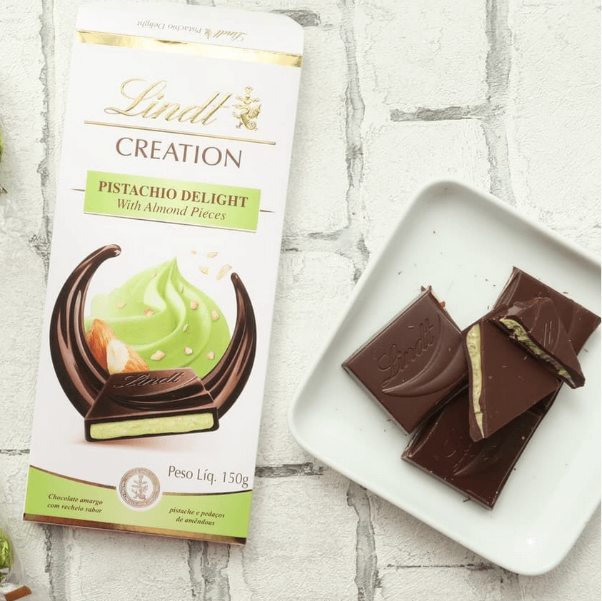 Lindt Creation pistachio and almond flavored chocolate packaging with chocolates on a white surface.