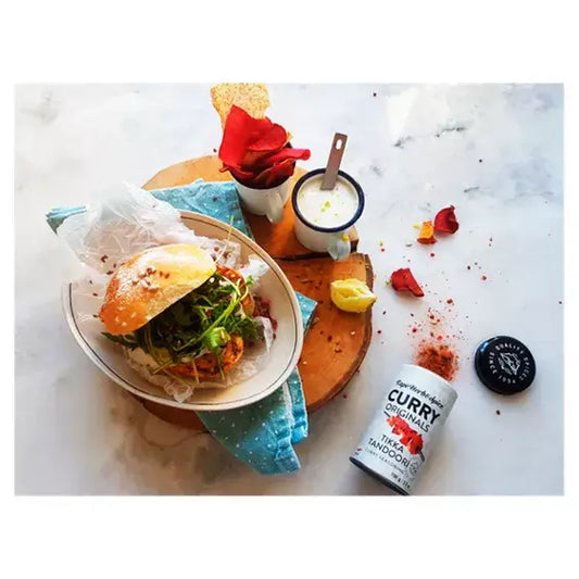 Delicious burger with fresh greens, Cape Herb & Spice Tikka Tandoori seasoning, and yogurt sauce on a rustic table.