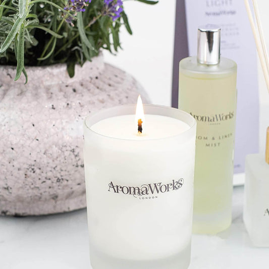 Aromaworks Light Range Petitgrain and Lavender Candle 75g glowing next to a diffuser and plant.
