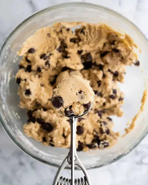 Bowl of chocolate chip cookie dough with a scoop, ready for baking homemade cookies.