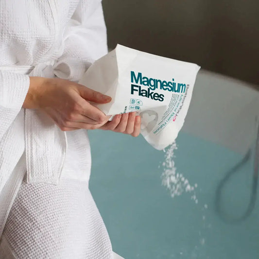 Person in a bathrobe pouring BetterYou Pure Magnesium Bath Flakes into a relaxing bath.
