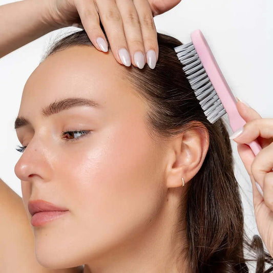 Woman using Brushworks HD Back Comb Brush for styling hair, showcasing its slender pin tail and nylon bristles.