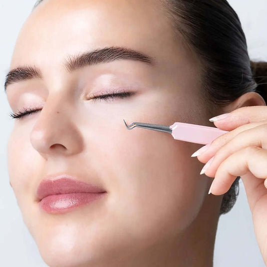 Model using Brushworks HD blackhead remover tool on clear complexion, showcasing stainless steel design and pastel handle.