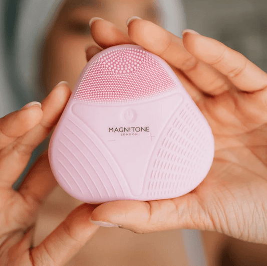 Magnitone XOXO SoftTouch Silicone Cleansing Brush in pink, held by a person for deep cleansing and gentle skin care.