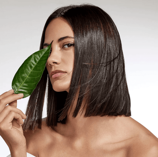 Model with sleek hair holding a green leaf, showcasing Aveda Botanical Repair™ Strengthening Leave-In Treatment.