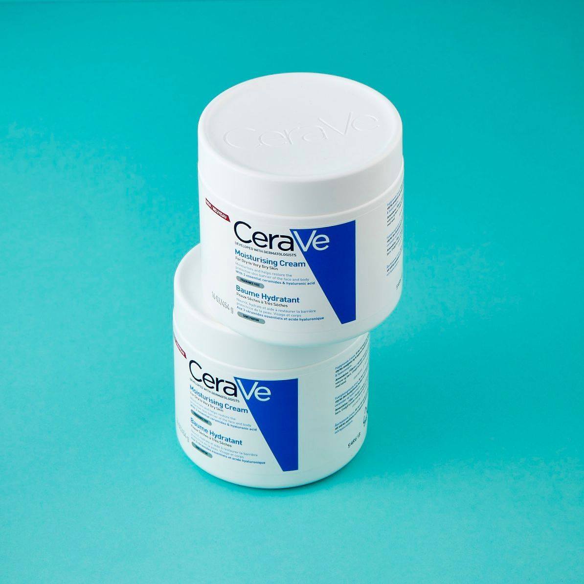 Two containers of CeraVe moisturizing cream stacked on a teal background