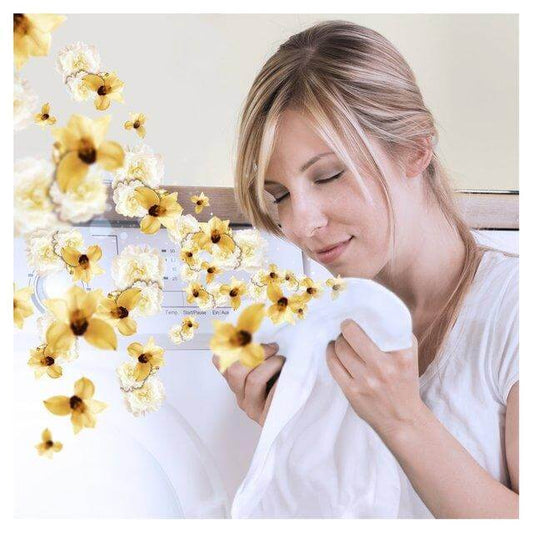 Woman enjoying fresh-smelling laundry with Lenor Gold Orchid scent booster, surrounded by yellow flowers.