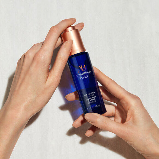 AUGUSTINUS BADER The Face Oil in blue bottle held by hands, ideal for radiant and youthful skin.