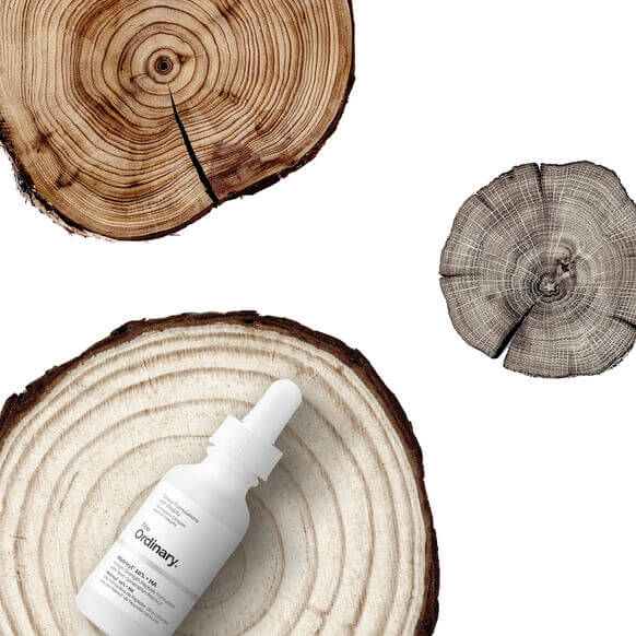 The Ordinary Matrixyl 10% + HA serum on wooden tree rings, showcasing a natural skincare aesthetic.