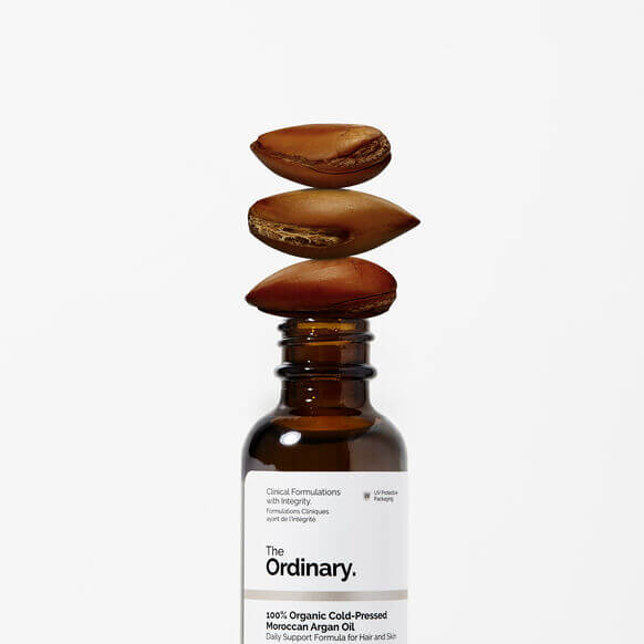 The Ordinary 100% Organic Cold Pressed Moroccan Argan Oil bottle with argan nuts stacked above, ideal for skin and hair hydration.