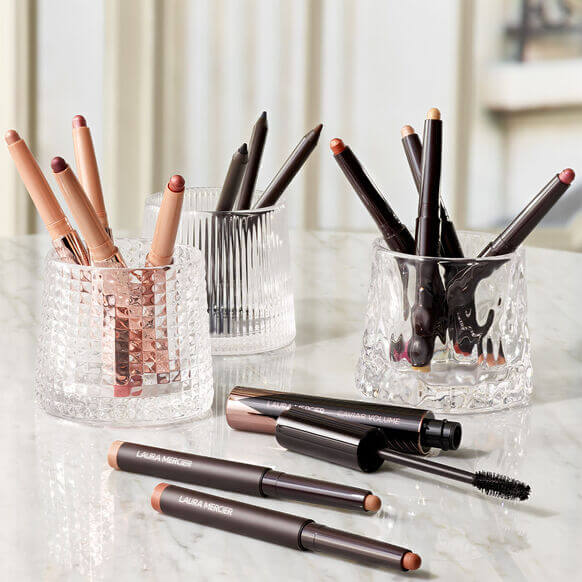 Laura Mercier Caviar Stick Eye Colour Matte shades displayed in crystal glass holders with mascara, showcasing elegant beauty.