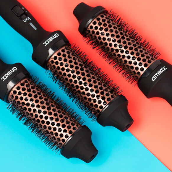 Amika Blowout Babe Thermal Brush with interchangeable barrel attachments for effortless styling on colorful background.