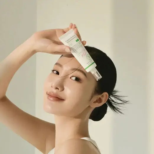 Smiling woman holding Axis-Y 6+1+1 Dark Spot Correcting Glow Serum against her forehead.