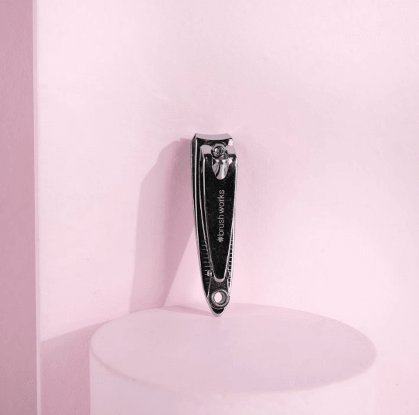 Brushworks Nail Clipper on a pink background, showcasing its stainless steel design for easy nail care at home.