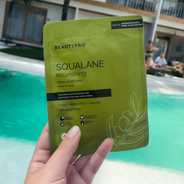 Person holding BeautyPro SQUALANE Nourishing Facial Sheet Mask packaging near a swimming pool.