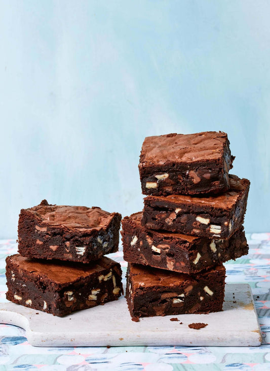 Stack of rich, fudgy brownies packed with chocolate chunks on a cutting board.