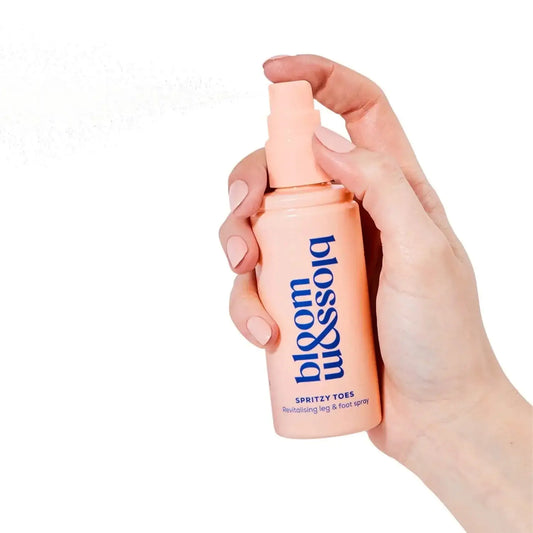 Hand holding Bloom and Blossom Spritzy Toes revitalising leg and foot spray 100ml in a pink bottle.