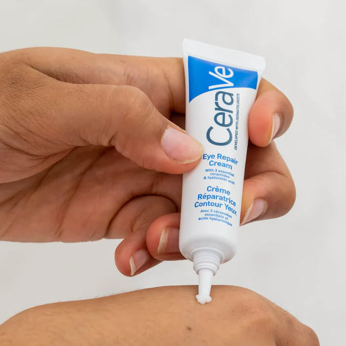 Hand holding a tube of CeraVe Eye Repair Cream against a white background