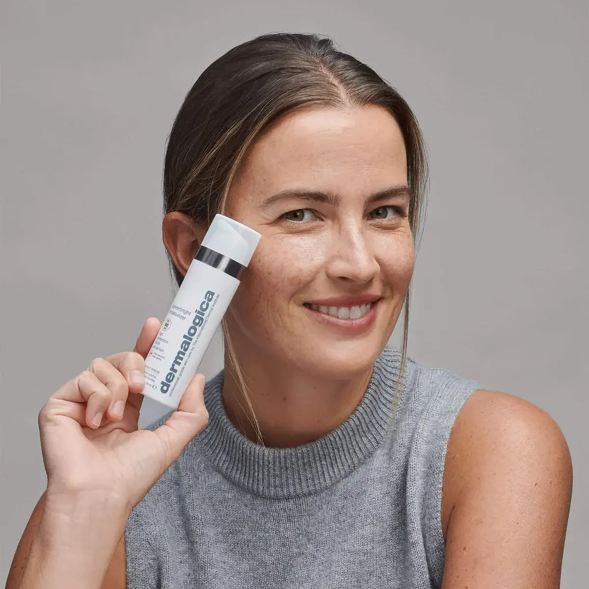 Woman holding a Dermalogica product against a gray background