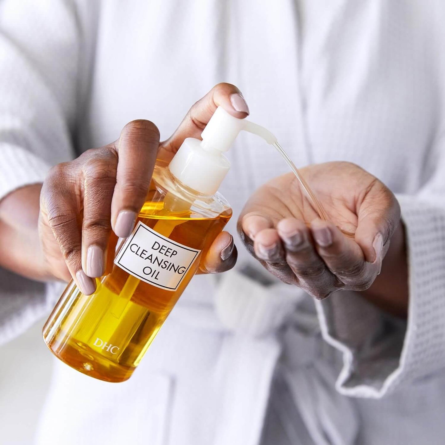 Person holding a bottle of DHC deep cleansing oil with a dropper.