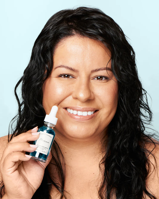 Woman holding a bottle of Earth Harbor skincare product against a light blue background