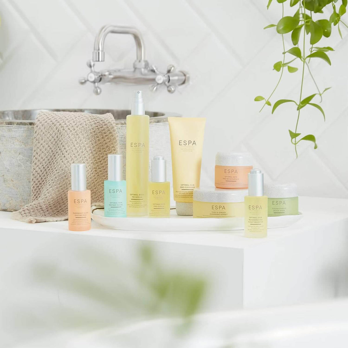 Collection of ESPA products on a bathroom counter with a bathtub and plant in the background.