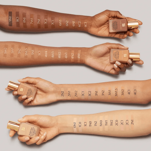 Various skin tones showcasing Estée Lauder Double Wear Foundation shades on arms with bottles in display.