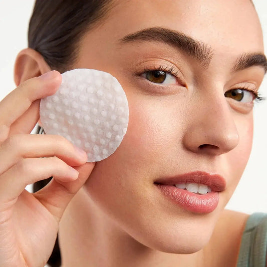 Model holding First Aid Beauty Facial Radiance Pad, promoting brighter skin with glycolic and lactic acids.