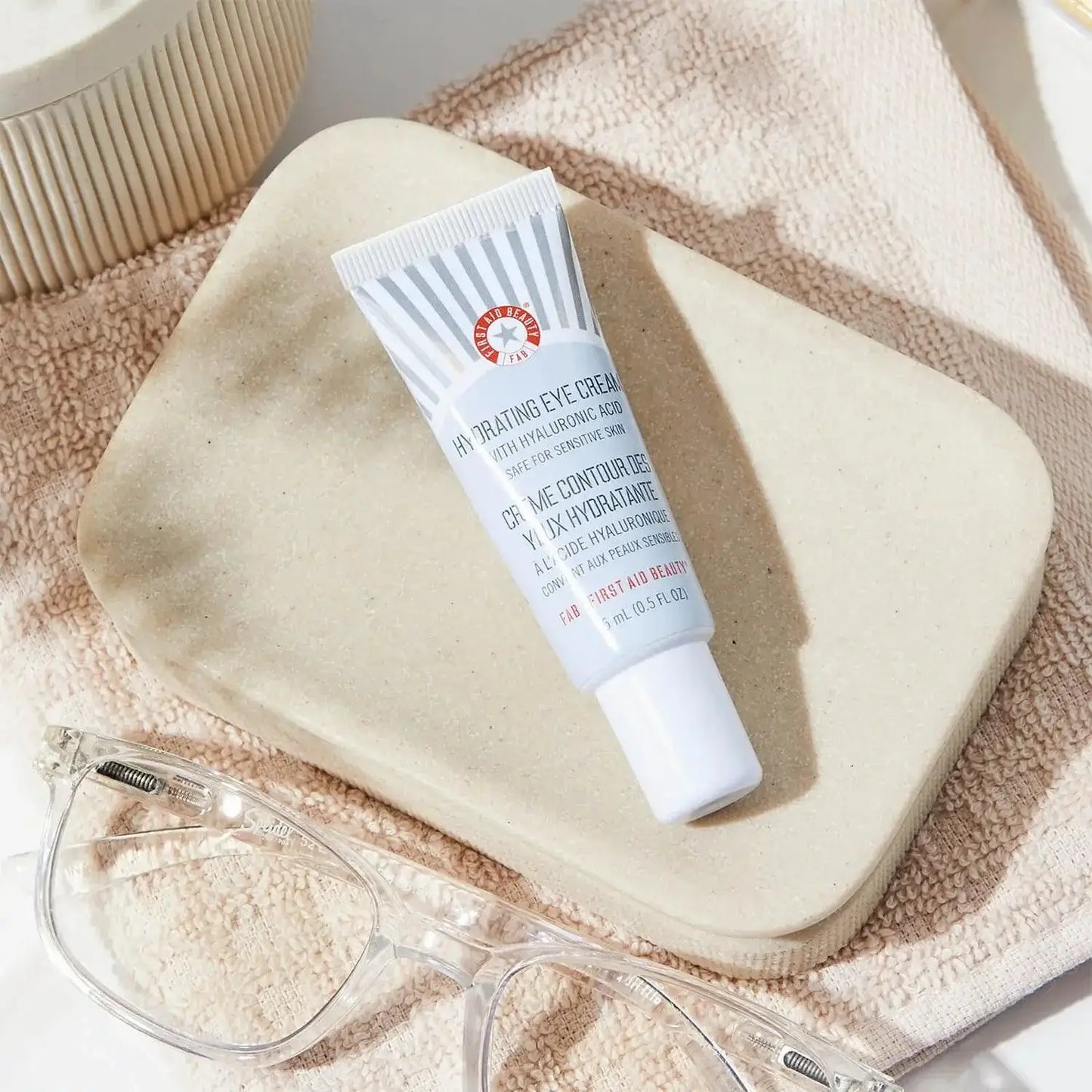 First Aid Beauty Hydrating Eye Cream 15ml tube on a beige plate, designed to moisturize and reduce puffiness.
