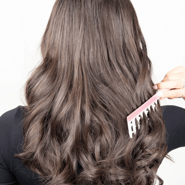 Woman using Brushworks Smoothing Curl Comb to create defined, bouncy curls in her long, wavy hair.