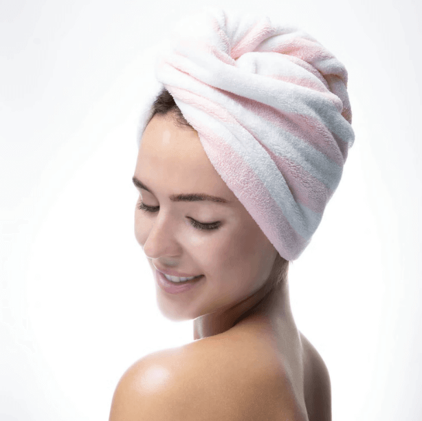 Woman with a pink and white luxury hair towel wrapped, featuring a twist design, smiling and showcasing smooth, frizz-free hair.