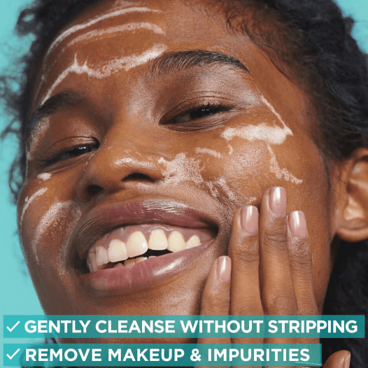Woman smiling with cleansing foam on her face, showcasing gentle cleansing and makeup removal benefits.