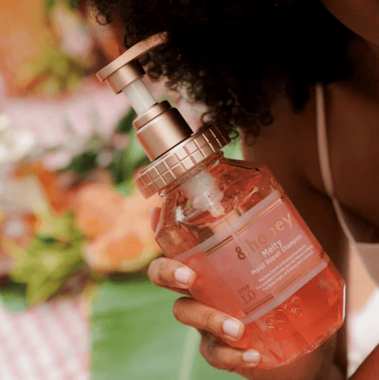 Hand holding a bottle of '&honey' hair product with a blurred floral background