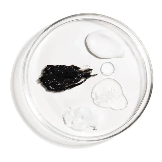 Close-up of various skincare products' textures including black, clear, and white creams on a glass dish.