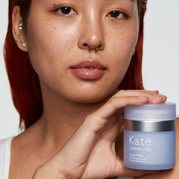 Woman holding a Kate Somerville product with a neutral background
