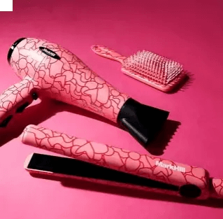 Mark Hill Love Is In The Hair Glam Kit with pink hairdryer, straightener, and brush on a pink background.