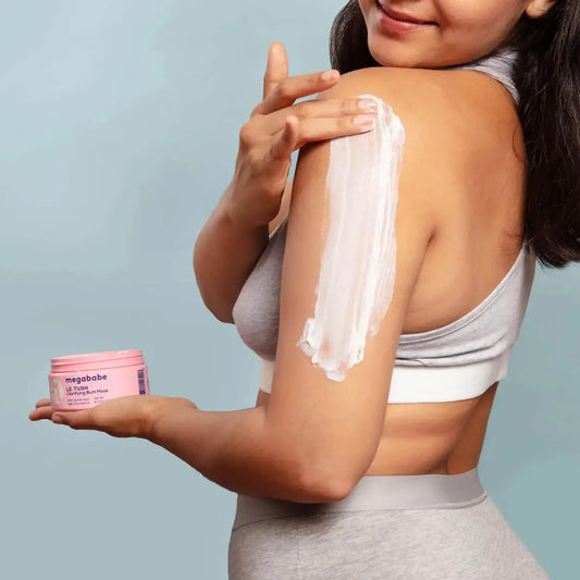 A woman applying Megababe Le Tush Clarifying Butt Mask on her shoulder for smooth skin.
