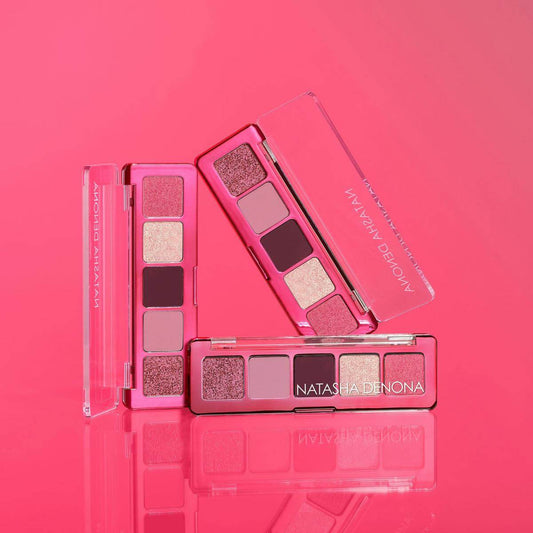 Natasha Denona Makeup palettes with shades of pink, red, and gold on a pink background