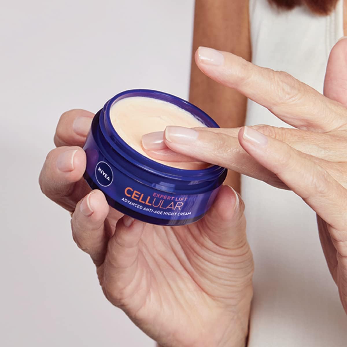 Person holding a Nivea cellular night cream jar with a neutral background