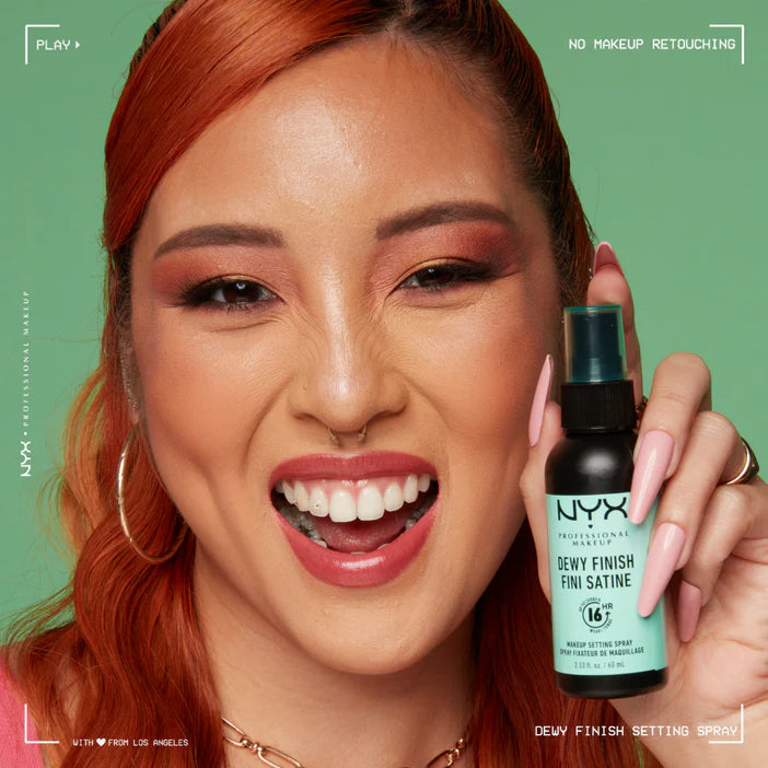 Woman holding a NYX Dewy Finish Setting Spray against a green background